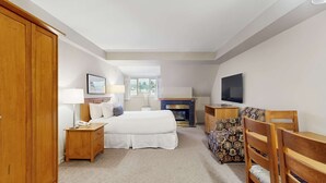 Una habitación de hotel con cama, mesita de noche, lámpara, televisor y un sofá estampado.
