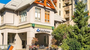 A building with a sign reading 'Whistler Peak Lodge,' featuring a prominent entrance with a porch, potted plants, and a bicycle parked outside.