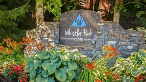 Une pancarte en pierre sur laquelle est inscrit « Whistler Peak Lodge », entourée d’une végétation luxuriante et de fleurs.