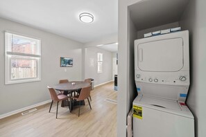 A modern kitchen with a built-in dishwasher, a dining area with a round table and chairs, and a view of the outside through a window. - Short North 2br, 2 Kings and Free Parking (Columbus)