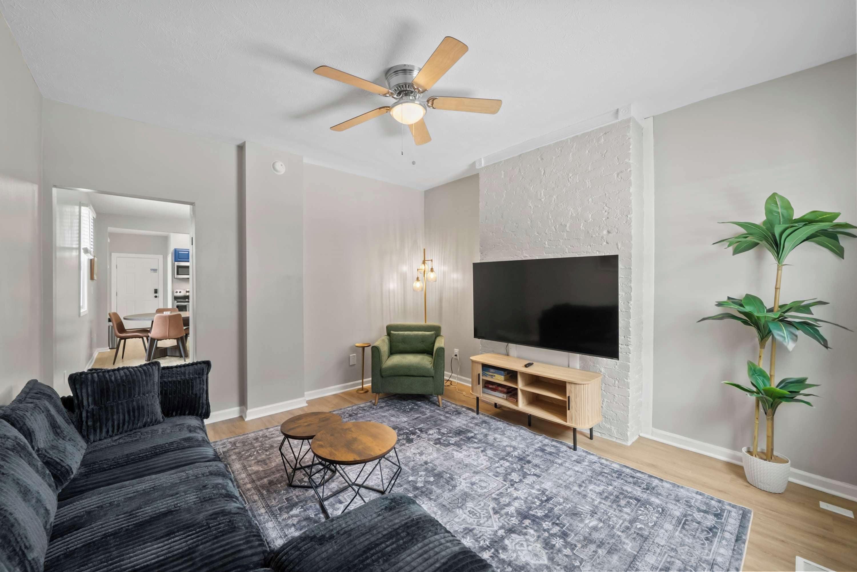 Een moderne woonkamer met een modulaire bank, een flatscreen televisie, een plafondventilator en een eethoek op de achtergrond.