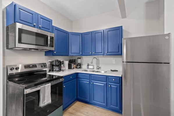 A modern kitchen with blue cabinets, stainless steel appliances, and a wooden floor. - Short North 2br, 2 Kings and Free Parking (Columbus)