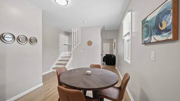 Un espace repas moderne avec une table ronde et quatre chaises, un escalier menant à un autre niveau et un tableau abstrait accroché au mur.