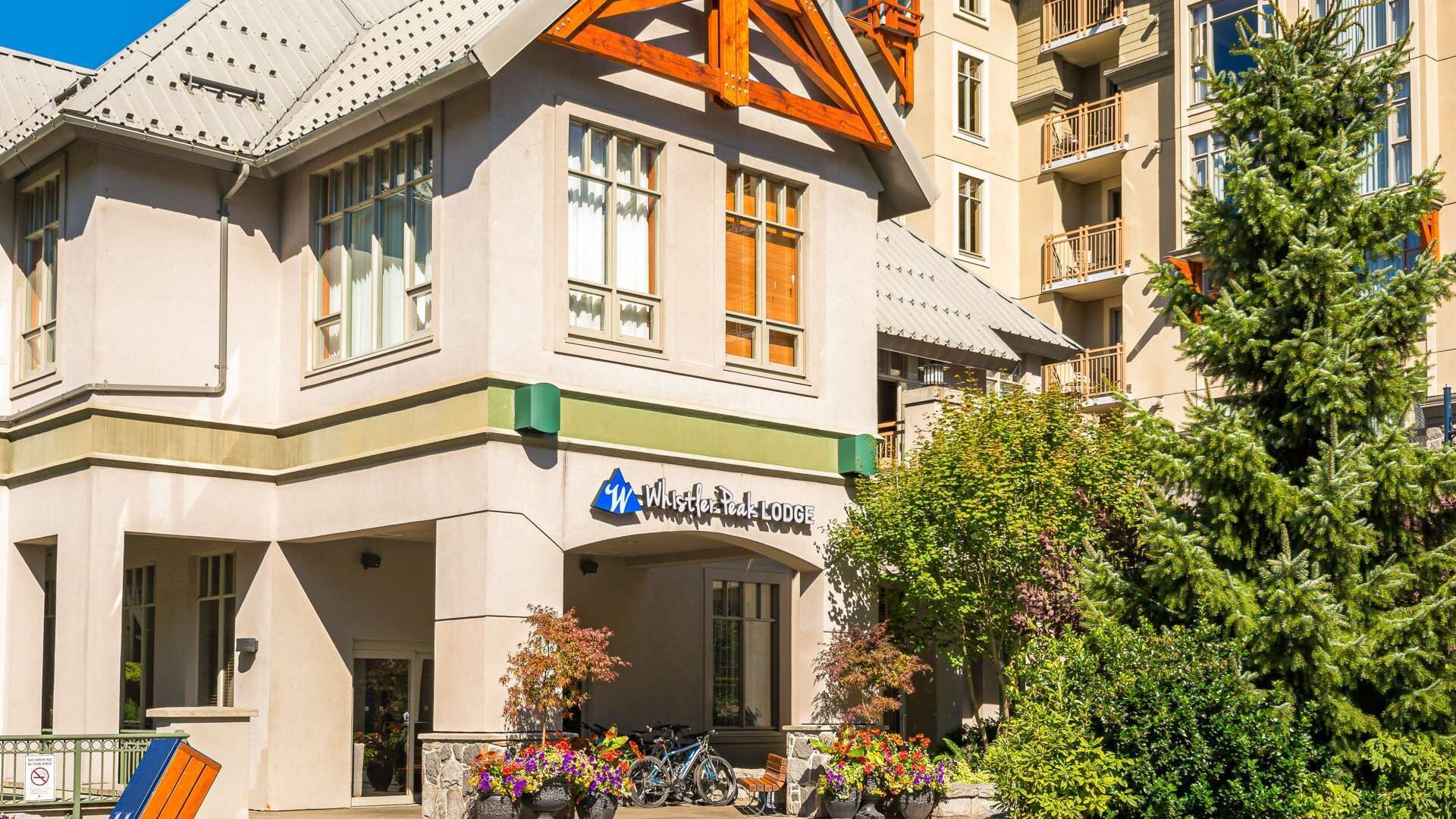 Un bâtiment sur lequel on peut lire l’inscription « Whistler Peak Lodge », avec une entrée imposante dotée d’un porche, de plantes en pot et d’un vélo garé à l’extérieur.