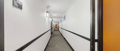 A hotel hallway with a carpeted floor, white walls, and a door on the right.