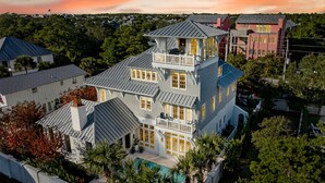 Een groot, meer verdiepingen tellend huis met een opvallend balkon, een zwembad en een weelderige tuin.
