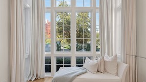 Een kamer met een groot raam, een witte bank en uitzicht op groen en een gebouw.