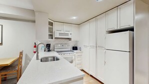 A modern kitchen with white cabinetry, a stainless steel sink, a microwave, a stove, and a refrigerator.