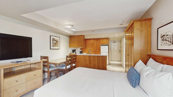 Quarto de hotel com cama, televisão, secretária, cadeira, cozinha compacta e guarda-roupa.