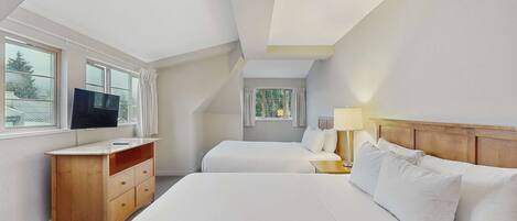 Habitación de hotel con dos camas, televisión, escritorio y ventana.