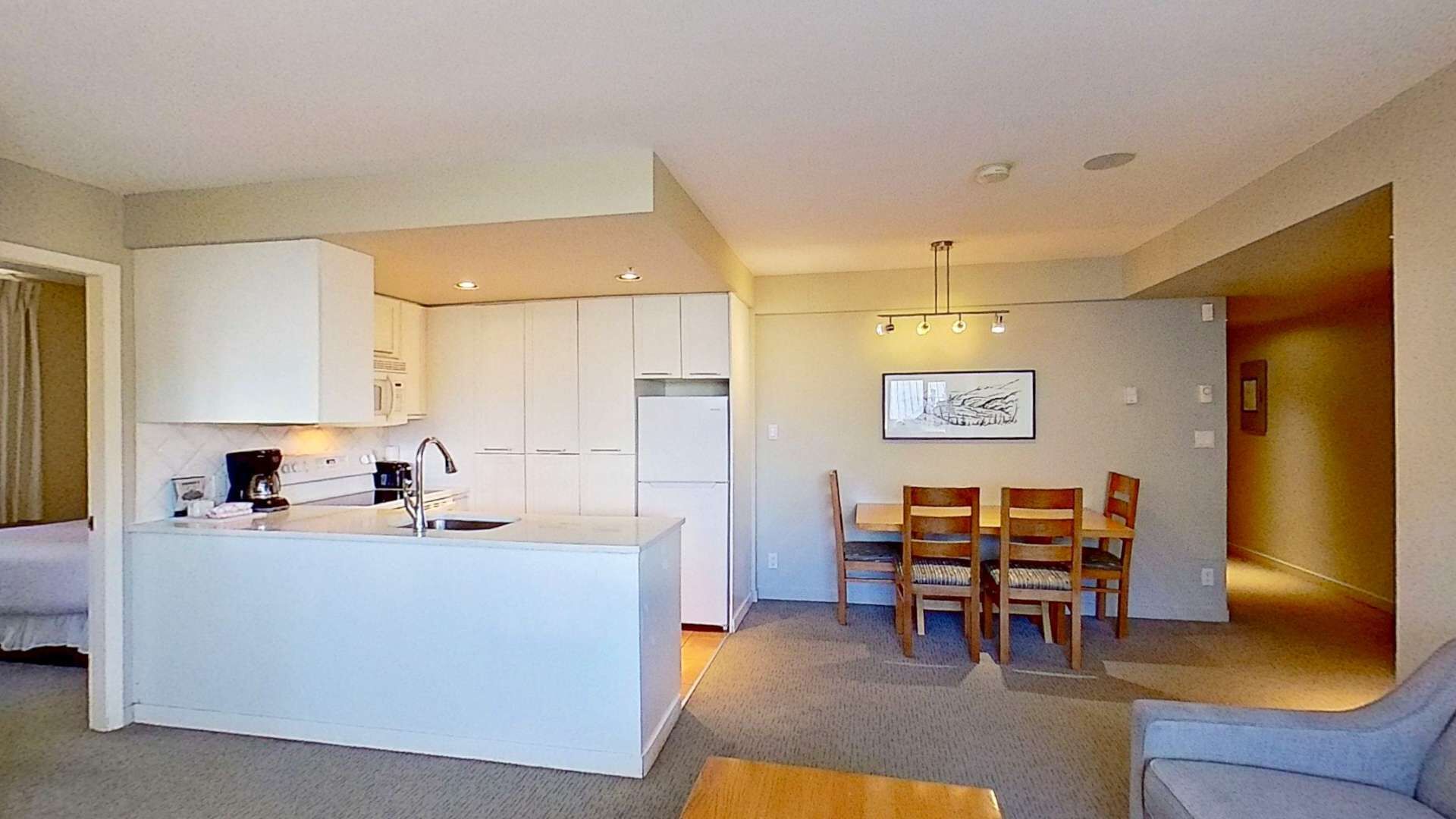 Et moderne køkken med hvide skabe, en central ø og et spiseområde med træstole og et bord.