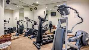 Un gimnasio con diferentes máquinas de ejercicio, incluyendo cintas de correr y elípticas, y un muro con espejos.