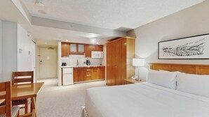 Habitación de hotel con cama, escritorio, silla, kitchenette y un cuadro en la pared.