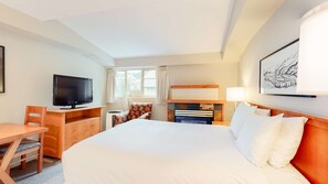 Ein Hotelzimmer mit einem großen Bett, einem Schreibtisch mit Fernseher, einem Sessel, einem Kamin und einem Vorhangfenster.