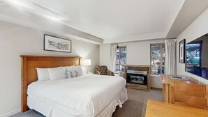 Habitación de hotel con una cama grande, un escritorio, una silla, una chimenea y una ventana con vista a árboles.