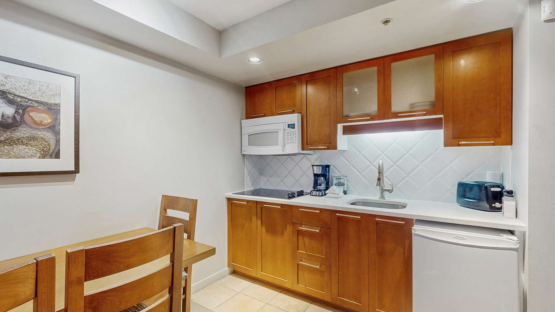 Una cocina compacta con armarios de madera, microondas, cafetera y refrigerador.