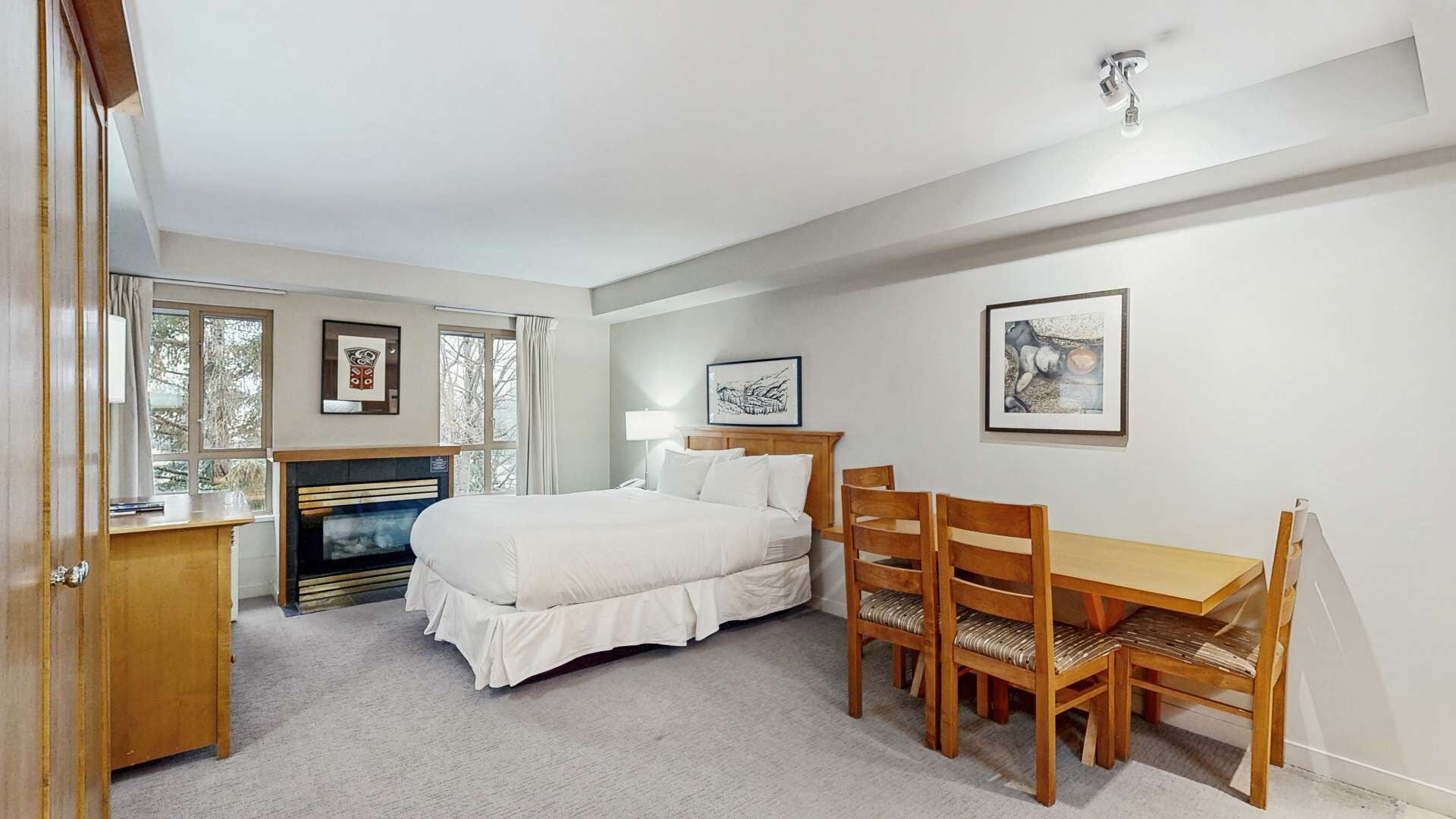 A bedroom with a bed, a desk, a chair, a fireplace, and framed artwork on the walls.