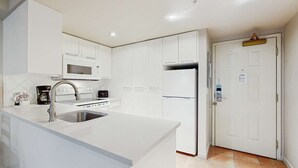 Una cocina moderna con armarios blancos, un lavamanos de acero inoxidable, un microondas, una cafetera y un refrigerador.