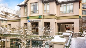 Ett hotell med en skylt som visar texten ”Whistler Peak Lodge”, och som består av en byggnad i flera våningar med stora fönster och en snötäckt fasad.