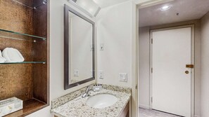 Ein Badezimmer mit Marmorplatte, Waschbecken, einem großen Spiegel und einem Glasregal mit Toilettenartikeln.