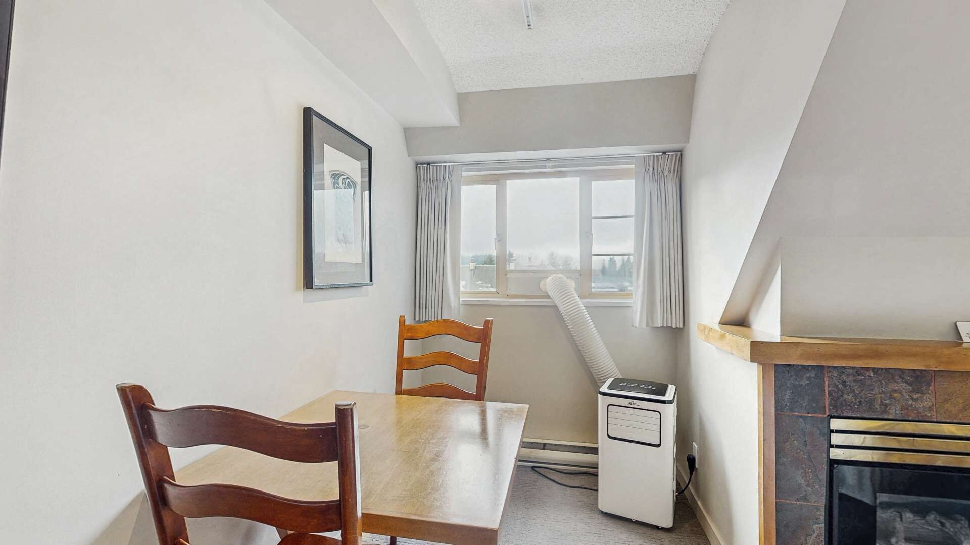 A small, cozy room with a dining table, two chairs, a radiator, a fireplace, and a window with curtains.
