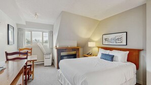 Habitación de hotel con cama, escritorio, silla, chimenea, ventana y un cuadro en la pared.
