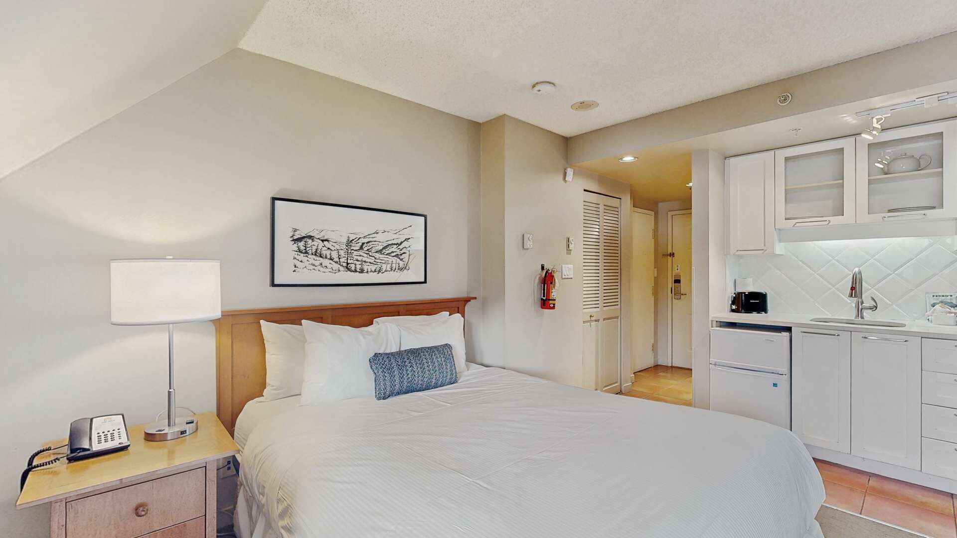 Quarto de hotel com cama, mesa de cabeceira, abajur e um quadro na parede.
