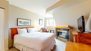 Una habitación de hotel con una cama grande, una chimenea, un televisor y obras de arte en las paredes.