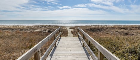 A wooden boardwalk leading to a beach with a clear sky.