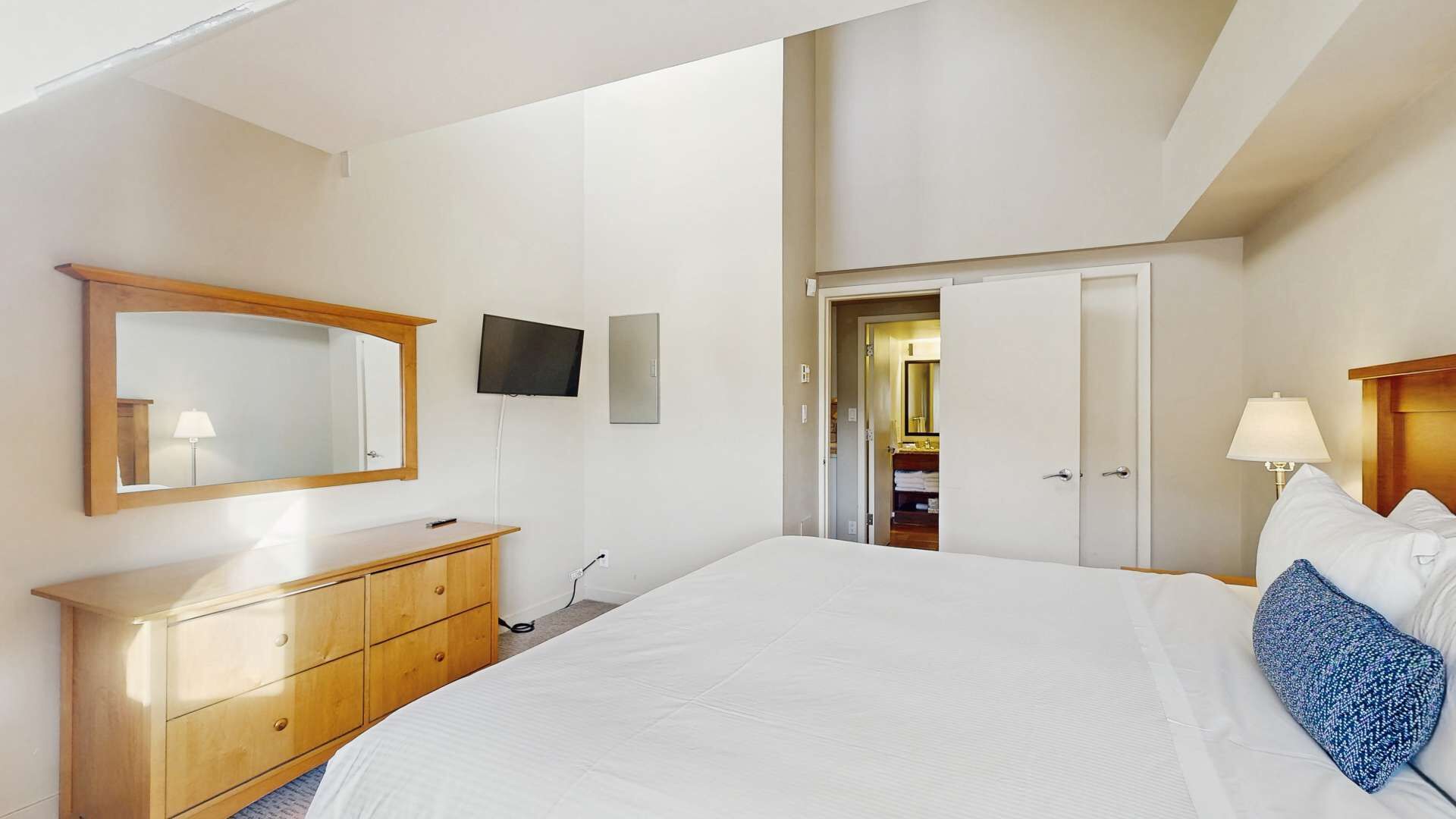Ein Schlafzimmer mit Bett, Schminktisch, Fernseher, Spiegel und einer Tür zum Badezimmer.