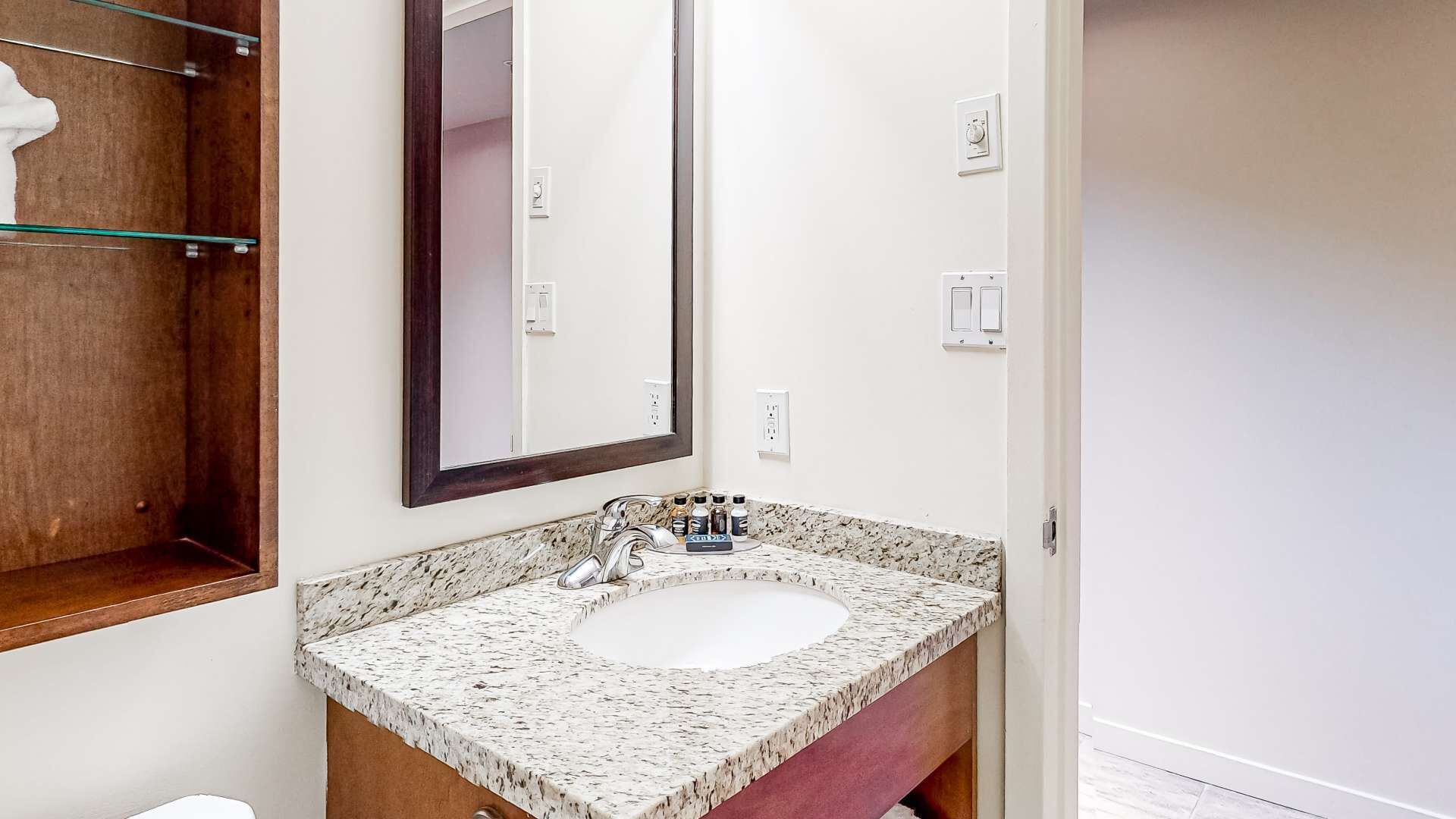 Un baño con lavamanos de encimera de granito, un espejo grande y un mueble de tocador de madera.