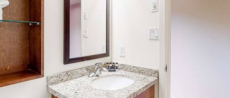 Un baño con lavamanos de encimera de granito, un espejo grande y un mueble de tocador de madera.