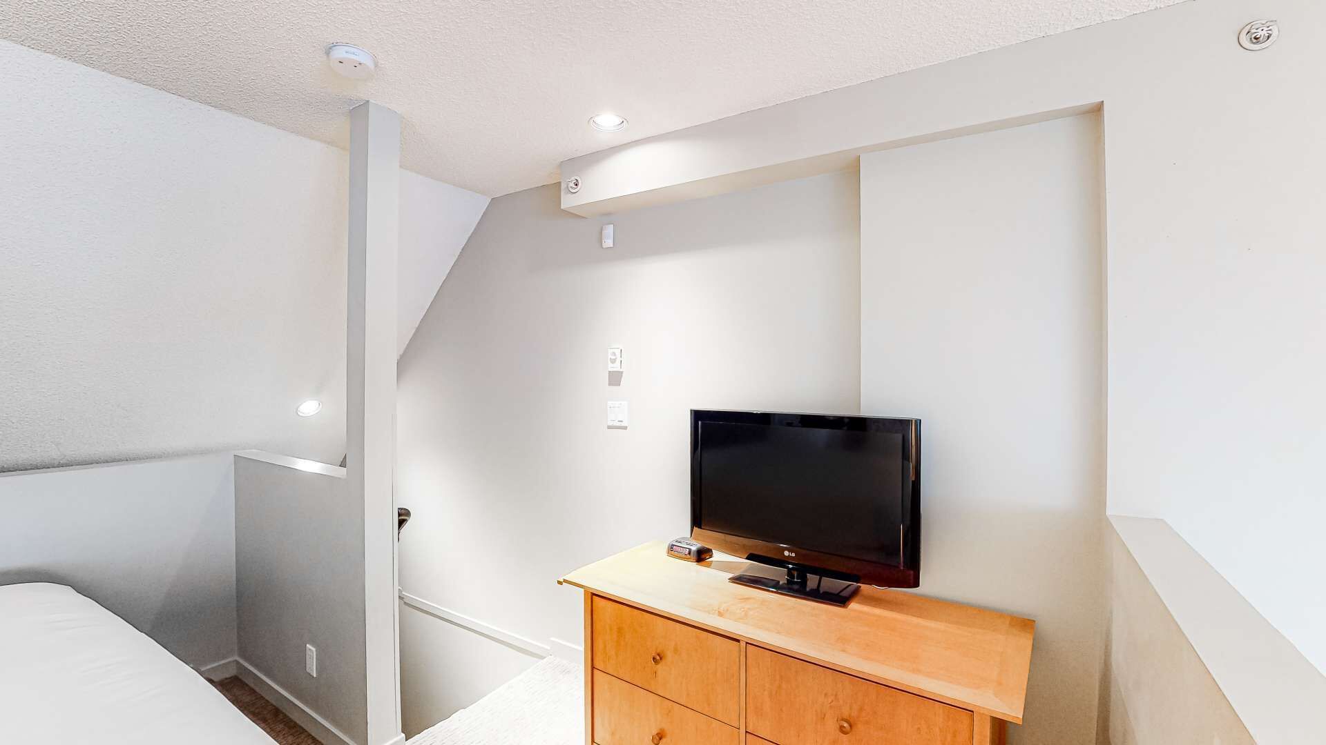 Ein modernes Schlafzimmer mit Flachbildfernseher auf einer Holzkommode, einer Treppe und Einbauleuchten.