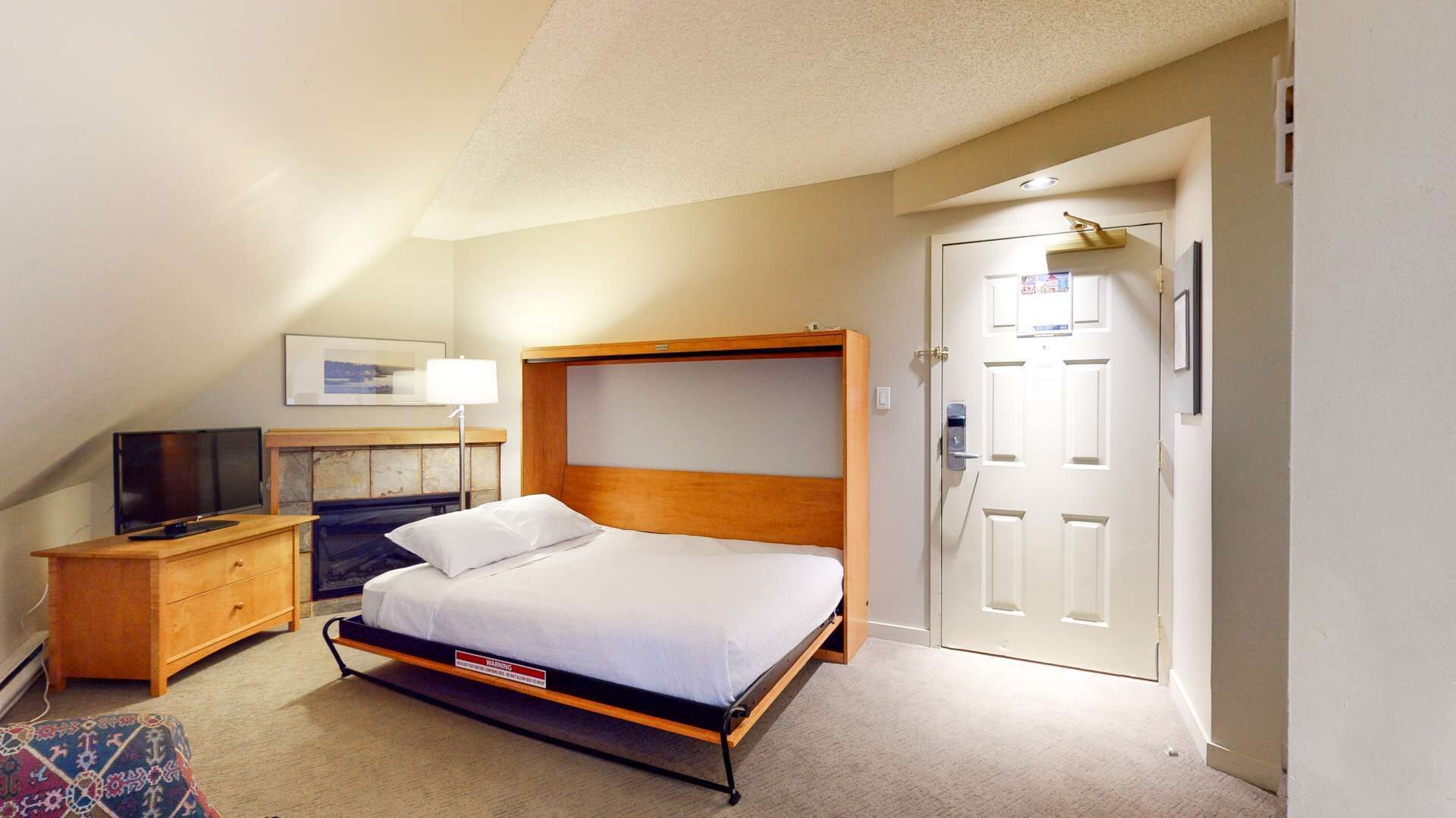 Ein Hotelzimmer mit Bett, Fernseher, Schreibtisch und Tür.