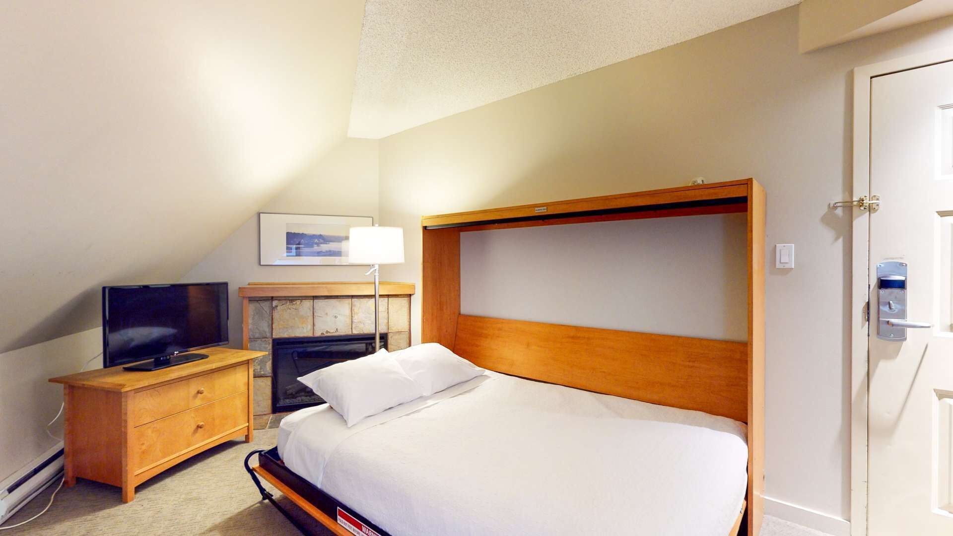 Ein Hotelzimmer mit einem Einzelbett, einem Holfnachtkästchen mit einem Fernseher, einem Kamin und einer Tür mit Schlüsselsperre.