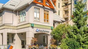 Rakennuksessa on kyltti, jossa lukee ”Whistler Peak Lodge”, ja siinä on parvekkeita sekä puutarha-alue, jossa on kukkia ja puu.