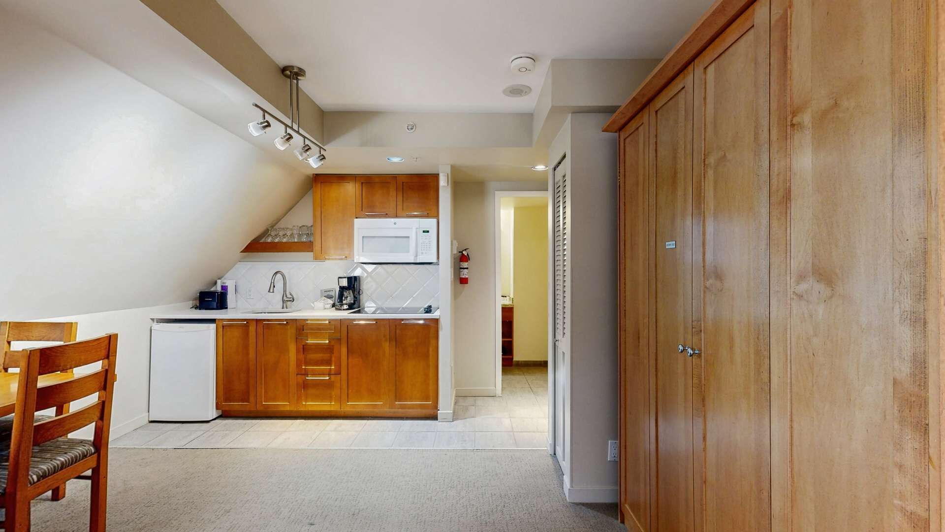 A compact kitchen with wooden cabinets, a microwave, and a small refrigerator.
