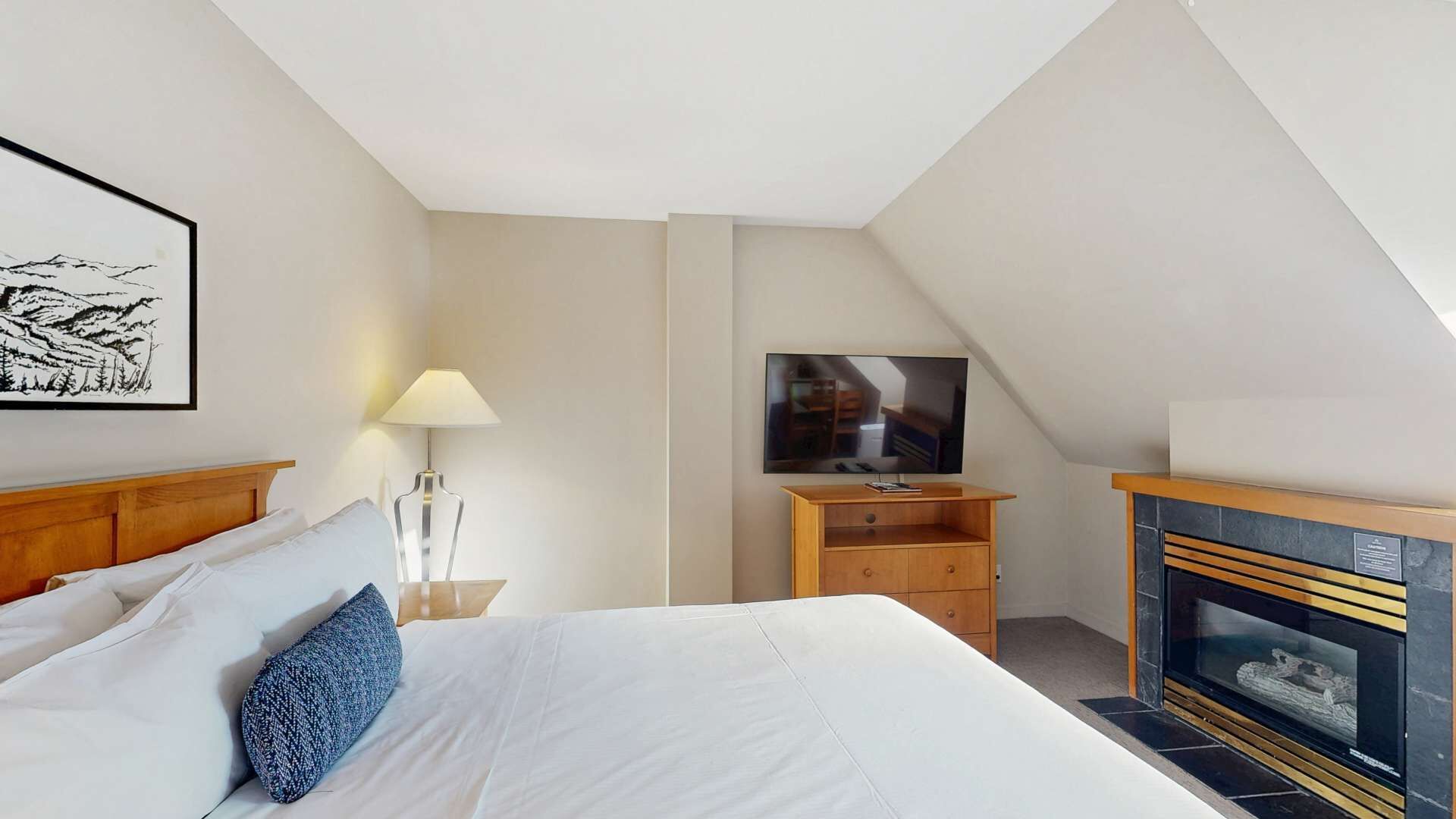 A bedroom with a bed, a TV, a fireplace, and a painting on the wall.