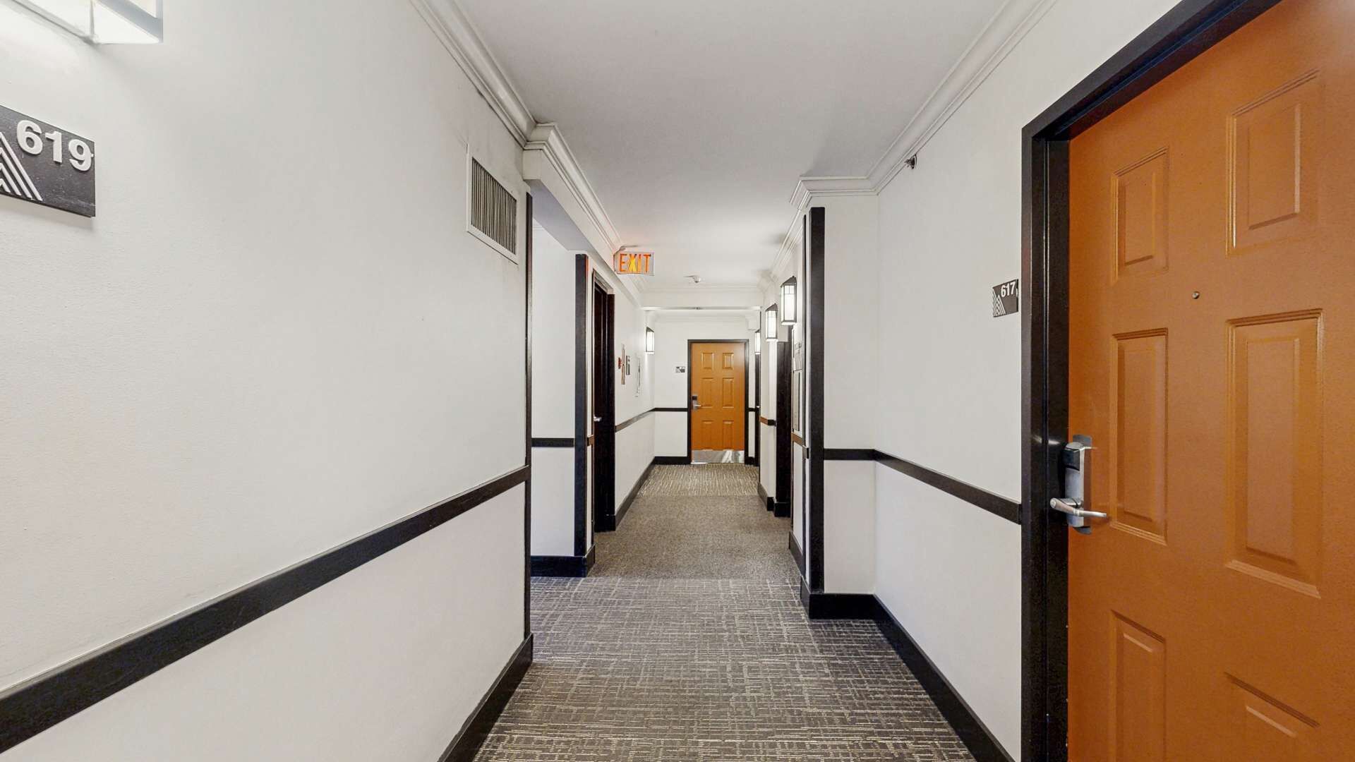 Pasillo de hotel con suelo alfombrado, paredes blancas y puertas numeradas 617 y 619.