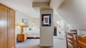 A bedroom with a bed, bedside tables, a desk, a chair, a heater, and a framed picture on the wall. - Whistler - Whistler Peak Lodge 619 (Whistler)