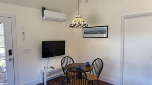 A dining area with a table, chairs, a TV, and a pendant light. - Cosy Red Cottage in Private Village On VT-100 (5-min to Mount Snow) (West Dover)