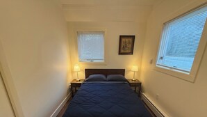 A bedroom with a bed, two bedside lamps, a window with blinds, and a picture on the wall. - Cosy Red Cottage in Private Village On VT-100 (5-min to Mount Snow) (West Dover)