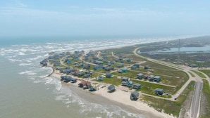 An aerial view of a coastal residential area with houses along the beachfront and a road curving through the landscape. - Bailey Beach House Beach Views (Freeport)
