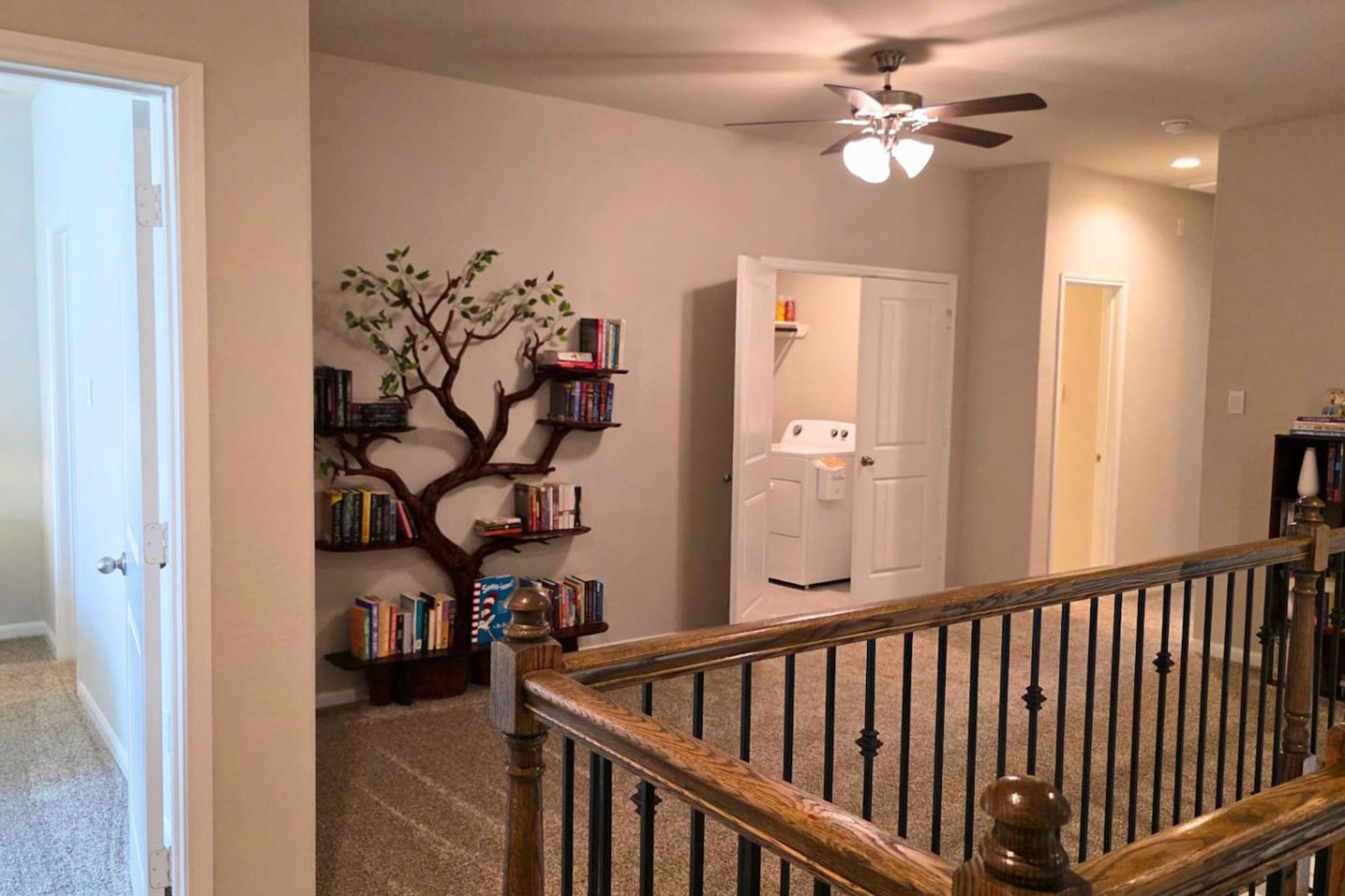 A home interior with a staircase, a ceiling fan, a bookshelf, and a door.
