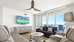 A modern living room with a large TV, a ceiling fan, a sofa, a coffee table, and a view of the ocean. - Silver Beach 0306e 3 Bedroom Condo (Destin)