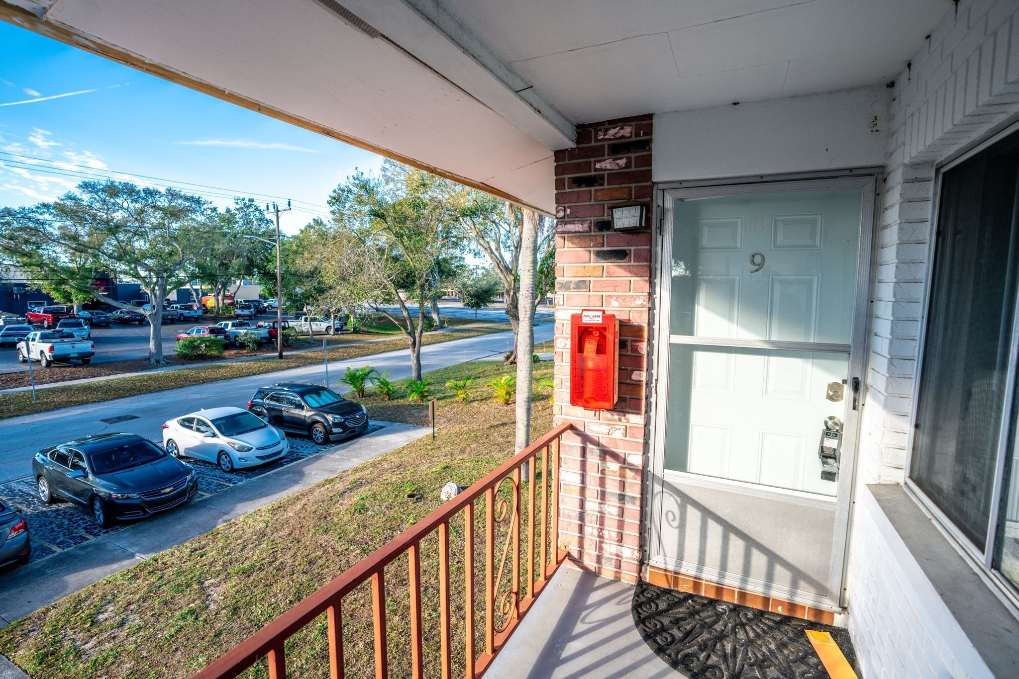 A covered porch with a brick wall, a white door marked with the number 9, and a red mailbox.
