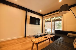 Un salon moderne avec un plancher en bois, un canapé en cuir noir, une table basse en bois et un téléviseur fixé au mur.