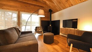 Ein gemütliches Wohnzimmer mit Holzbalkendecke, einer Couch, einem Sessel, einem Fernseher und einem Kamin.