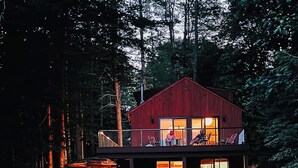 Eine zweigeschossige Holzhütte mit Balkon, umgeben von Wald und Teich.