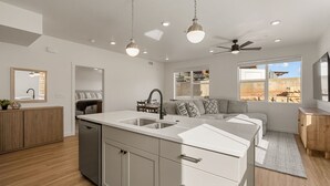 A modern kitchen with a central island, a dining area, and a living space with a sofa and a TV.